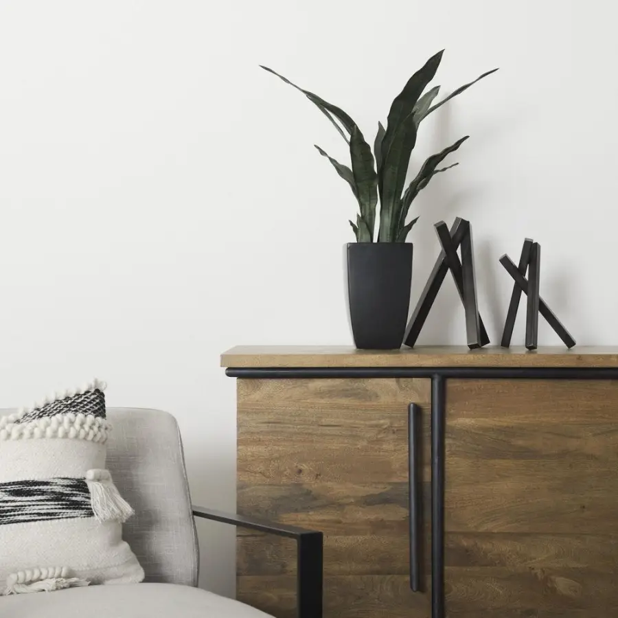 Gunmetal gray abstract metal sculptures on a wood sideboard beside a potted plant